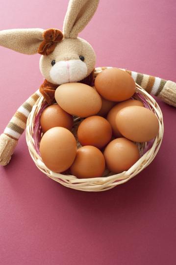easter_egg_bowl.jpg - Cute little soft toy Easter bunny with a wicker basket full of fresh brown eggs over a red background in a high angle view