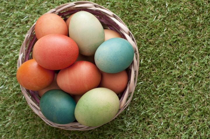 basket_of_colouredeaster__eggs.jpg - Close-up from above view of wicker basket full of colored easter eggs over green lawn grass background with copy space