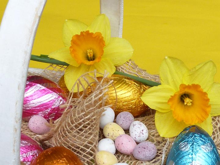 easter_basket_flowers.jpg - Easter basket with fresh yellow narcissus flowers in spring, colorful chocolate eggs and quail egg candies in rustic sack cloth against yellow background