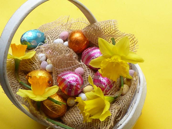 easter_decorated_basket.jpg - Easter decorated basket on yellow background with chocolate easter eggs collected into sack cloth with fresh daffodil flowers, viewed from high angle on vivid yellow background
