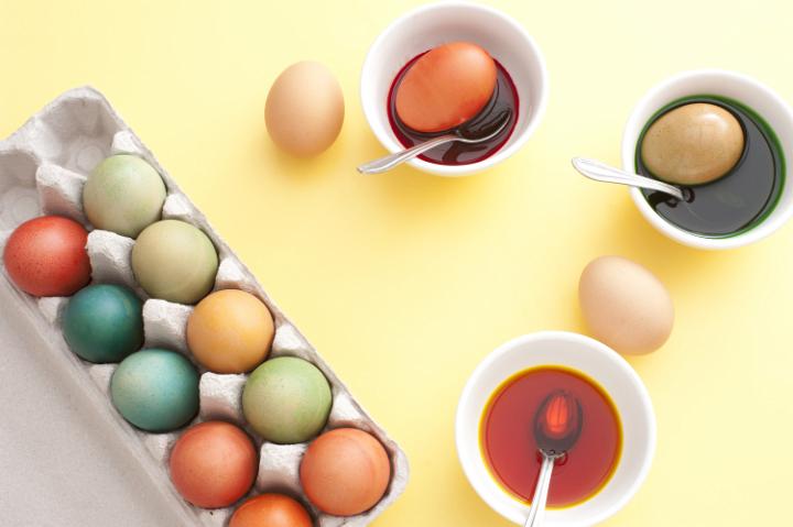 easter_egg_preparing.jpg - Childhood tradition dyeing boiled eggs for a festive Easter with an overhead view of bowls of dye and a cardboard box full of dyed completed eggs on a yellow background