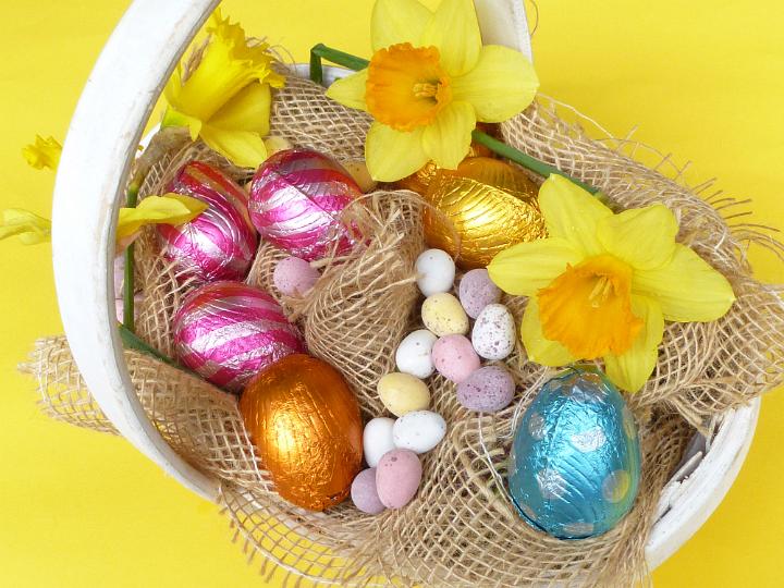 egg_hunt_basket.jpg - Easter egg hunt basket filled with assorted collected eggs nestling in hessian cloth decorated with spring daffodils