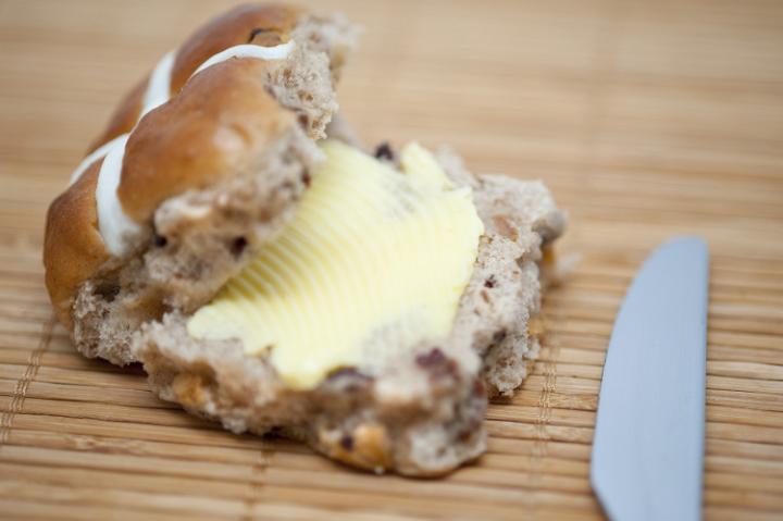 hotcross_bun.jpg - Closeup of a freshly baked buttered sliced Hot Cross Bun with a knife to celebrate Easter