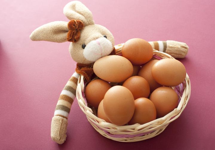 rabbit_basket_eggs.jpg - Stuffed plush toy Easter bunny with a basket of fresh brown hens eggs over a red background viewed from above
