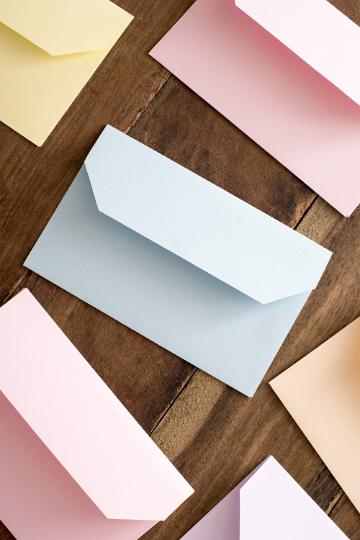easter_greeting_opened.jpg - Top view of several open pink, blue and yellow envelopes on brown wooden surface