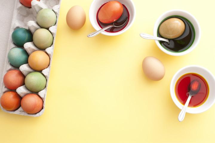 colouring_easter_eggs.jpg - Making traditional homemade dyed hens eggs for Easter steeping them in cups of colored dye with a cardboard carton of finished eggs alongside, overhead view with copy space