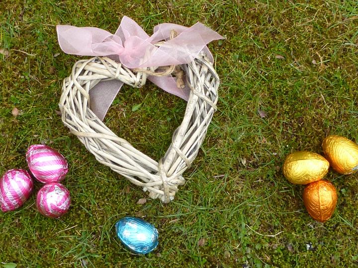 easter_love.jpg - Handcrafted wicker heart tied with a pink ribbon lying on grass with colorful Easter Eggs symbolic of Love at Easter