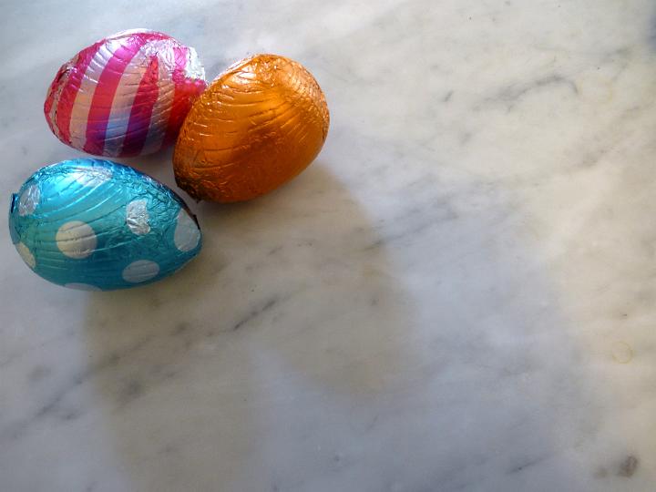 three_easter_eggs.jpg - Three chocolate Easter eggs wrapped in colorful aluminium foil in close-up on white marble surface with copy space