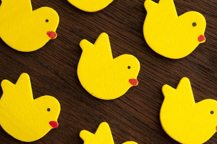 wooden_easter_chickens.jpg - Rows of colorful bright yellow Easter chicks forming a diagonal background pattern on a dark wood surface in a full frame view