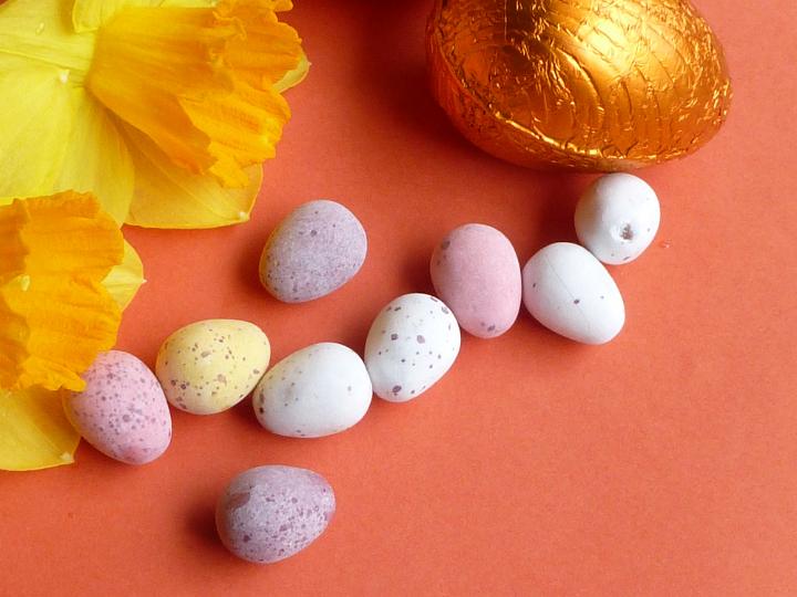 assorted_easter_eggs_red.jpg - Easter background of small mini sugar-coated and foil eggs with two colorful yellow spring daffodils on a textured orange surface with copy space
