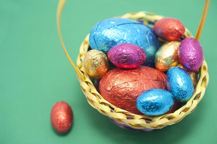 collected_easter_eggs.jpg - Collection of foil wrapped chocolate Easter Eggs of various sizes and colours collected in a basket on a green bakground