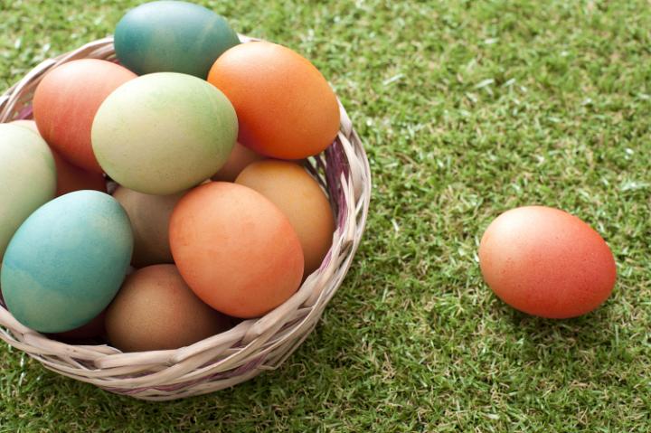 colourful_basket_of_eggs.jpg - Wicker basket filled with colorful dyed boiled Easter eggs on neat green grass with a single egg alongside and copy space