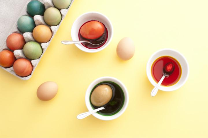 colouring_eggs.jpg - Overhead view of three bowls filled with dye beside a carton filled with colorful eggs