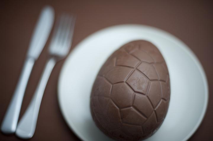 concept_chocolate_egg.jpg - Overhead close up view of one chocolate egg in small white bowl with fork and knife nearby