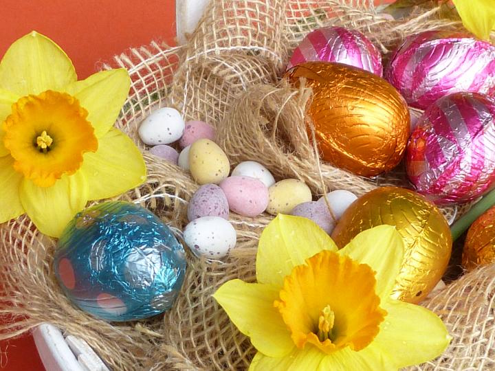 easter_basket_assortment.jpg - Easter basket assortment of sugar coated mini eggs, foil wrapped chocolate eggs and spring flowers with yellow daffodils on a base of hessian cloth