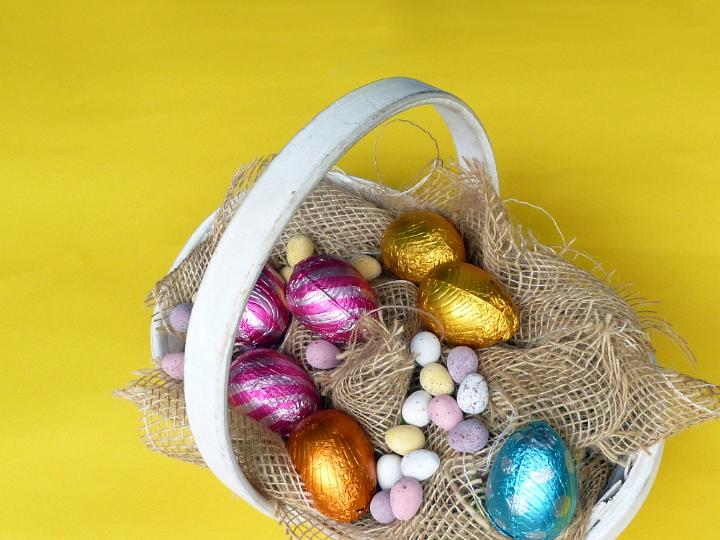 easter_basket_yellow.jpg - Basket with chocolate Easter eggs in colorful foil and colored mini quail eggs candies sitting on rough sack cloth, viewed from above against yellow background