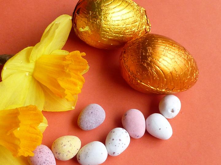 easter_egg_assortment.jpg - Assorted colorful foil and sugar-coated Easter eggs with yellow spring daffodils on a red background for a festive holiday background