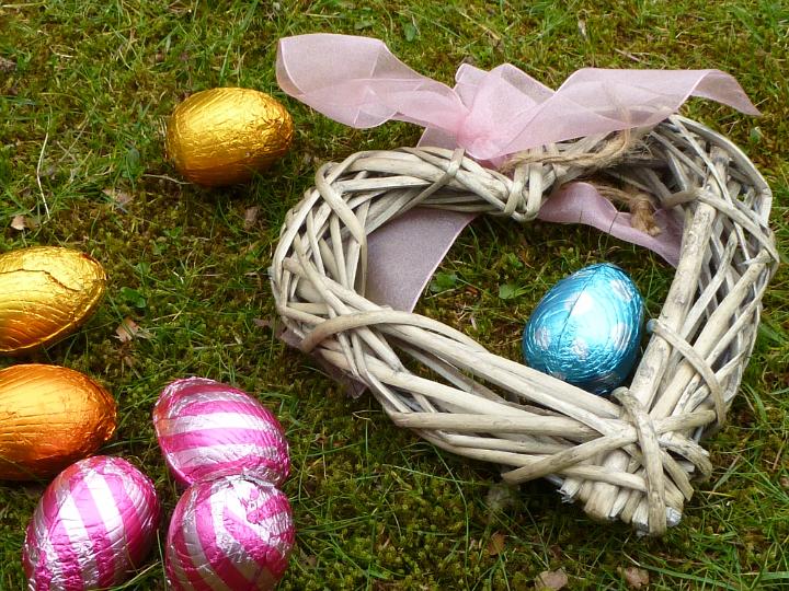 easter_love_heart.jpg - Handmade rustic wicker Easter heart decorated with a pink ribbon and bow for Love on green grass with foil wrapped eggs