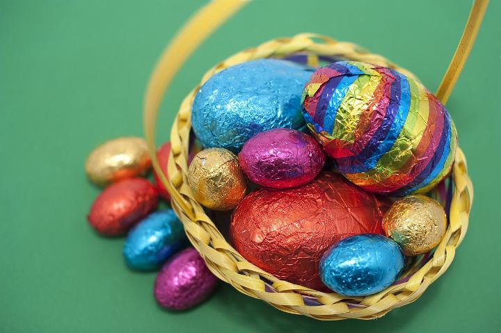 egg_basket_easter.jpg - Overhead view of a basket of colourful foil wrapped Easter Eggs on a green background