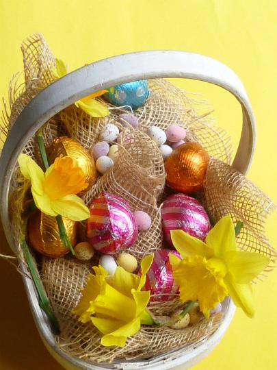 full_easter_basket.jpg - Easter basket filled with holiday goodies including colorful foil wrapped chocolate eggs, sugar-coated mini eggs and spring daffodils arranged in hessian