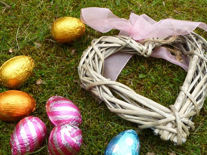 love_for_easter.jpg - Rustic hand made wicker heart tied with a pink ribbon lying on green grass with colorful chocolate foil Easter eggs symbolic of love at Easter