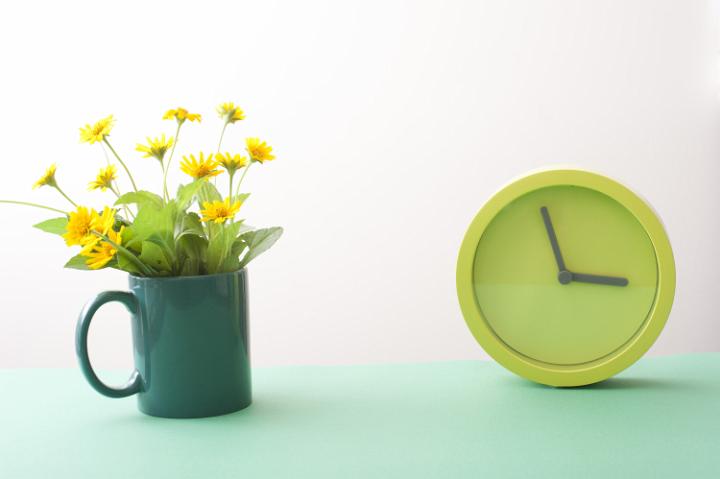 easter_time_background.jpg - Yellow spring flowers in green mug and simple round green watch on turquoise surface over white background. Easter time concept