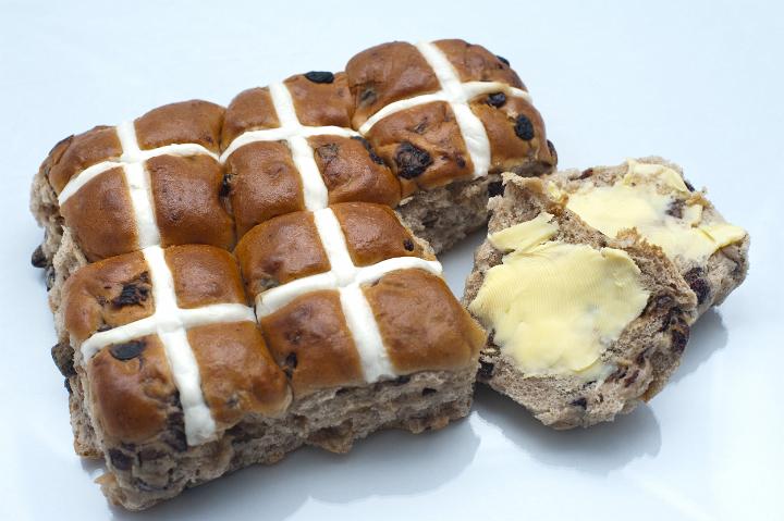 butter_hotcross_bun.jpg - Overhead view of a batch of fresh Easter Hot Cross Buns showing the glazed cross with one sliced and buttered one to the side