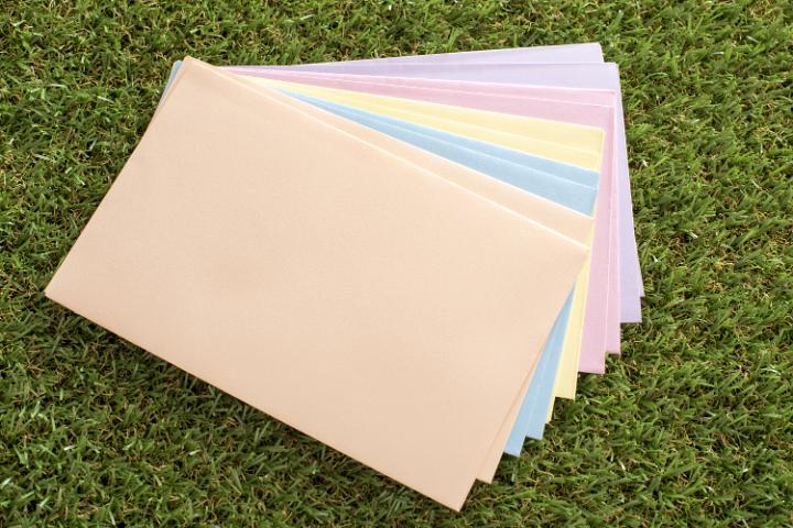messages_for_easter.jpg - Stack of colorful unused envelopes for Easter messages lying fanned out on fresh green grass in a concept of spring and holiday celebration greetings