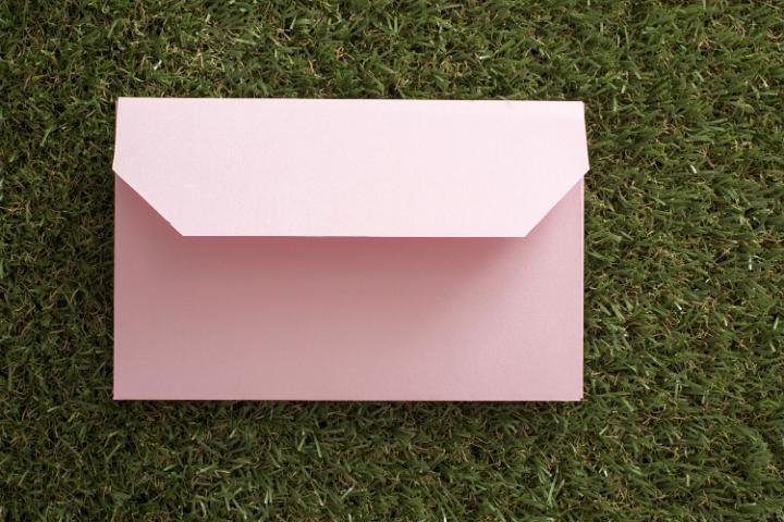 opened_envelope.jpg - Single pastel pink envelope opened face down on green grass conceptual of Easter spring greetings and wishes